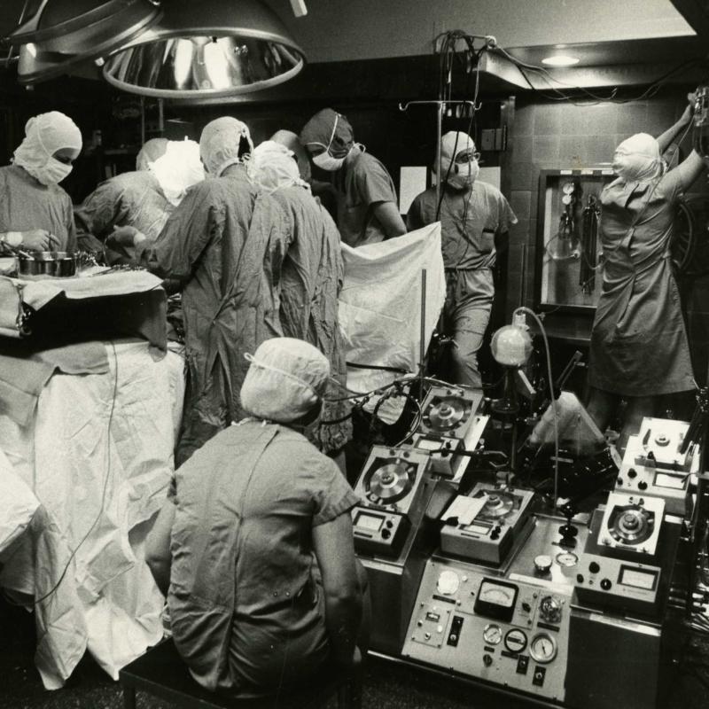 Open heart surgery with heart-lung machine in foreground, being monitored by a nurse